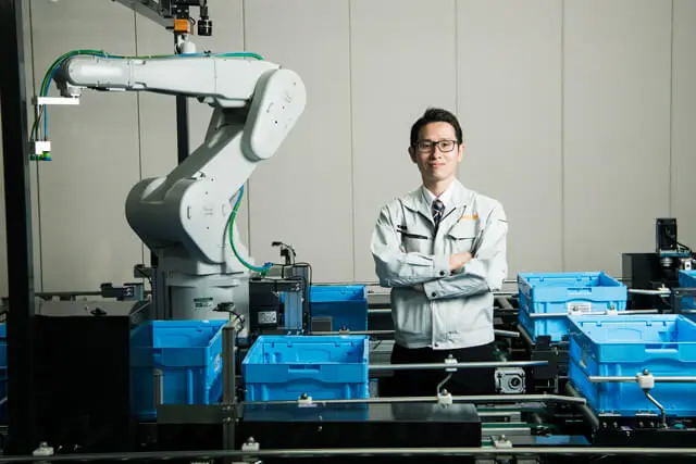 Mujin CEO and co-founder, Issei Takino, standing next to piece picking robot